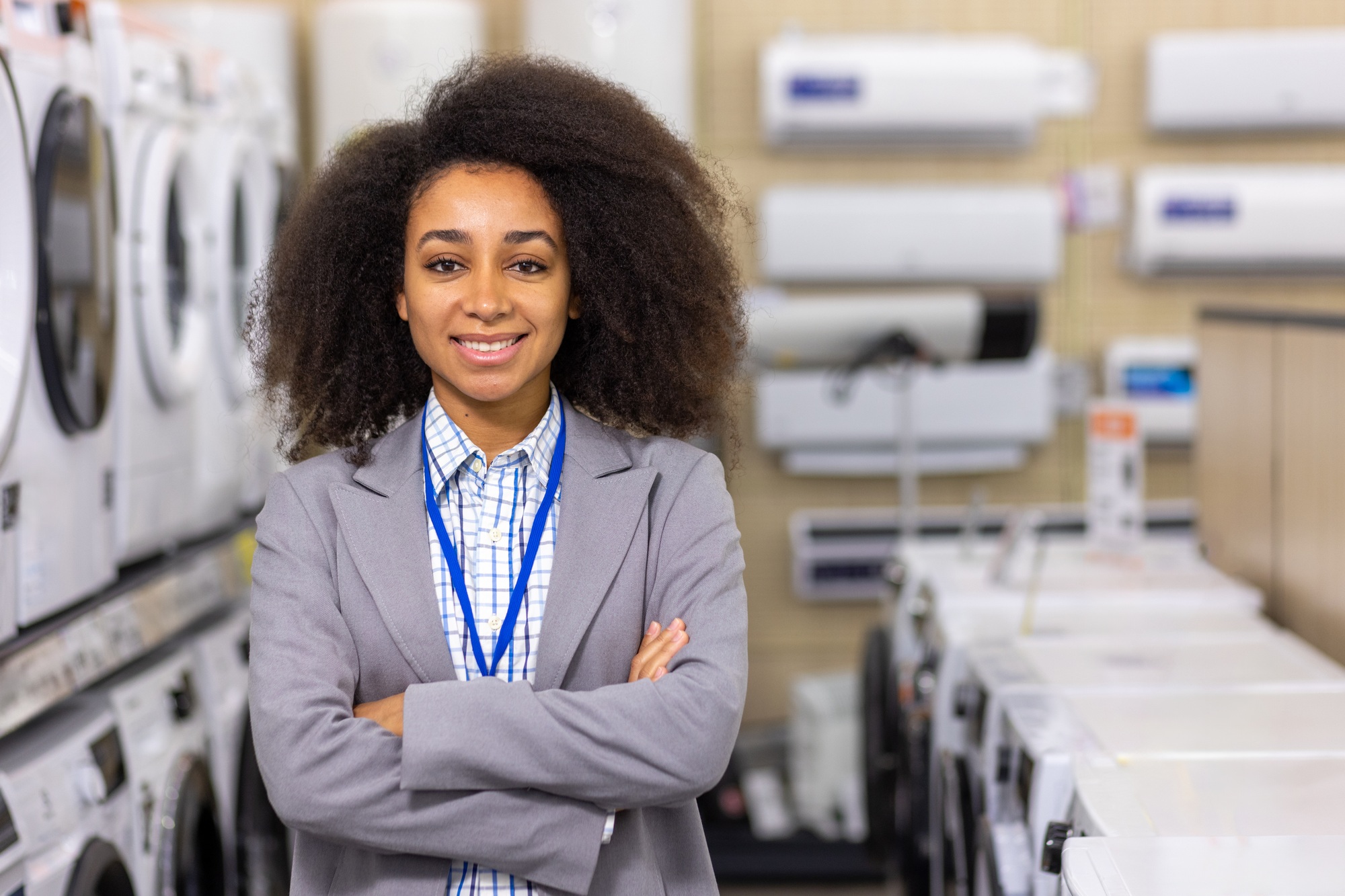 Confident saleswoman in a home appliance store standing with arms crossed, ready to assist