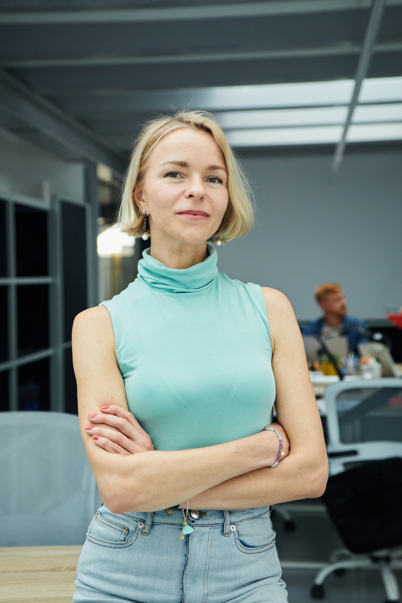 Vertical confident Caucasian business woman looking at camera standing with arms crossed in office.